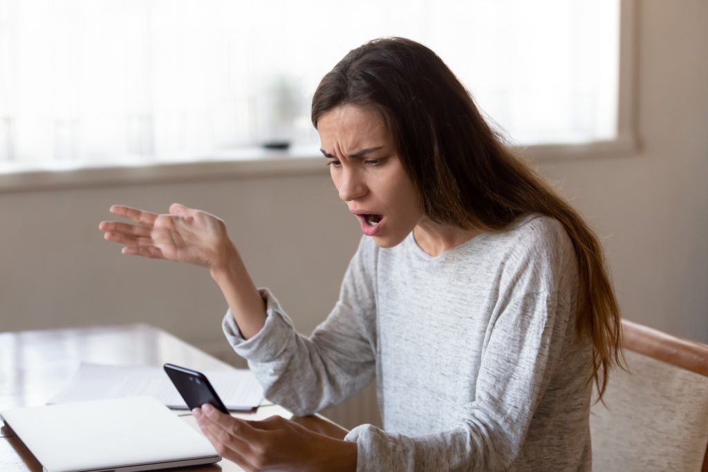 Angry young woman looking on mobile phone screen having problems